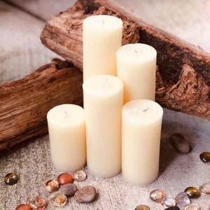 May include: Five ivory pillar candles of varying heights arranged in a pyramid shape on a rustic wooden surface. The candles are surrounded by small decorative stones.