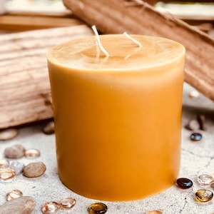 May include: A large, round, amber-colored candle with two white wicks. The candle is sitting on a light brown surface.