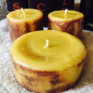 May include: Three yellow beeswax candles with brown flecks and white wicks. The candles are sitting on a white fluffy surface.