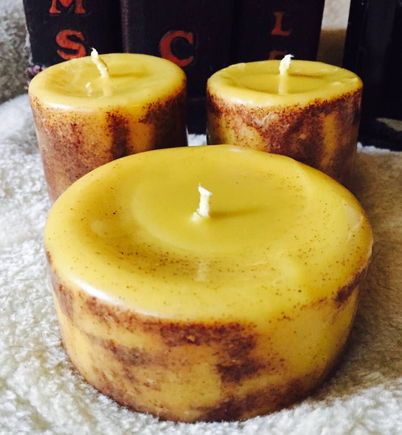 May include: Three yellow beeswax candles with brown flecks and white wicks. The candles are sitting on a white fluffy surface.