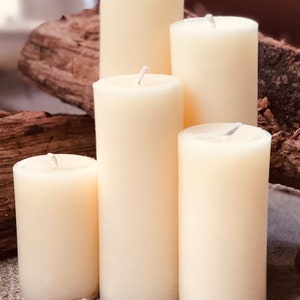 May include: Four ivory pillar candles of varying sizes arranged in a pyramid shape on a wooden surface. The candles are unlit and have a smooth, matte finish.