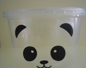 May include: A clear plastic container with a panda face design. The panda has black eyes, a black nose, and black ears.