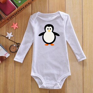 May include: White long-sleeved baby onesie with a cartoon penguin graphic. The penguin is black and white with orange feet.