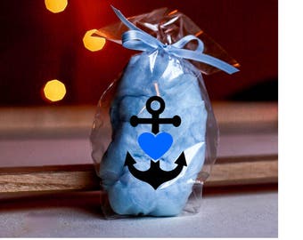 May include: A clear cellophane bag tied with a light blue ribbon contains blue cotton candy. A black anchor design with a blue heart is printed on the front of the bag. The background is a blurred red and brown.