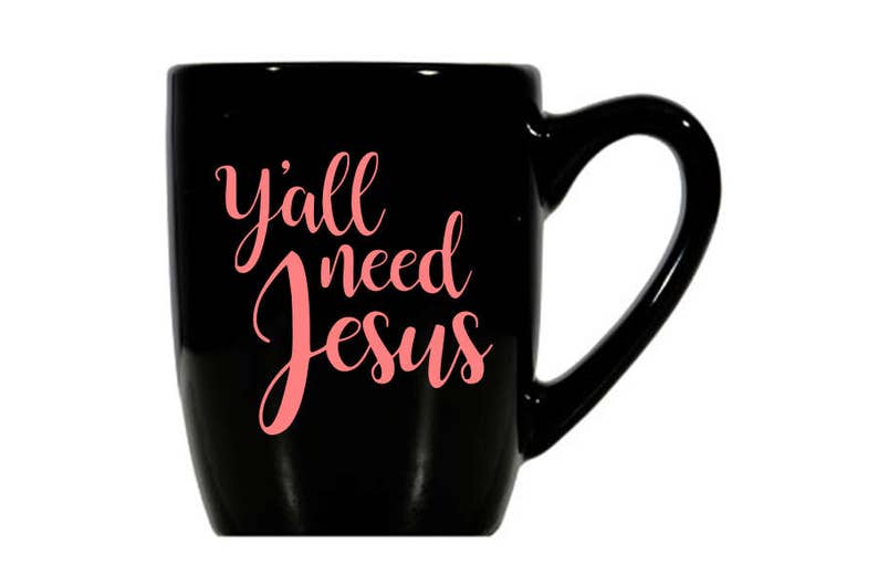 May include: Black ceramic coffee mug with a white handle. The mug has the text "y'all need Jesus" written in pink.