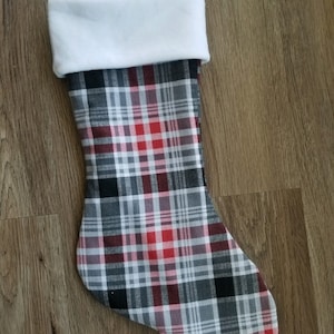 May include: A red, black, and gray plaid Christmas stocking with a white fleece cuff.