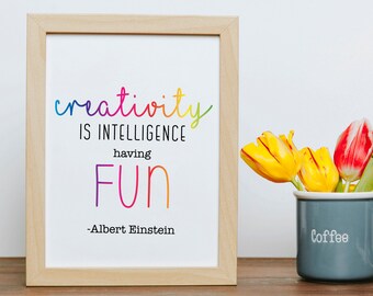 Op de afbeelding: Een ingelijst print met een citaat van Albert Einstein: "Creativiteit is intelligentie die plezier heeft." De quote is geschreven in regenboogkleuren en de lijst is van licht hout.