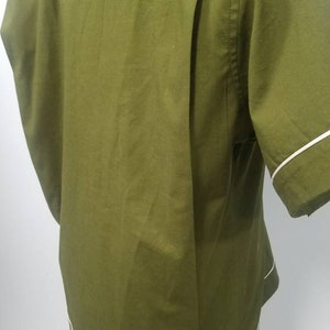 May include: Olive green short-sleeved shirt with white trim on the sleeves and hem. The back of the shirt features a pleated design. The shirt is buttoned at the bottom and is displayed on a mannequin.