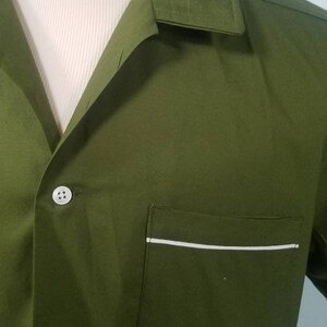 May include: Olive green button-down shirt with a notched collar and a chest pocket. The pocket is trimmed with a thin white stripe. The shirt is displayed on a mannequin.