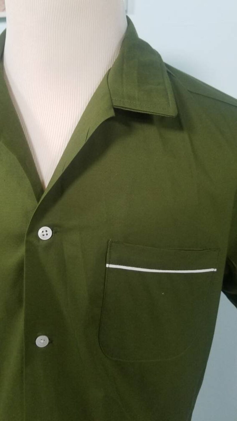 May include: Olive green button-down shirt with a notched collar and a chest pocket. The pocket is trimmed with a thin white stripe. The shirt is displayed on a mannequin.