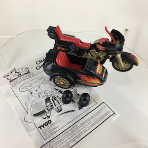 Może przedstawiać: Czarny i czerwony motocykl z bocznym wózkiem. Motocykl ma namalowane płomienie na bocznym wózku i napis "Born to Crash" na boku. Motocykl jest wyposażony w dwa czarne kaski.