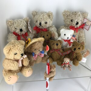 May include: A collection of plush teddy bears in various poses and outfits. Some bears are wearing red, white, and blue patriotic themed accessories. The bears are arranged on a glass shelf with a red pen in the foreground.