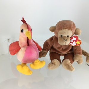 May include: Two Ty Beanie Babies, a pink and red rooster and a brown monkey. The monkey has a red tag with a white star and the words "Ty Beanie Babies" on it.