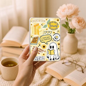 May include: A clear phone case with a yellow background and various book-themed stickers. The stickers include stacks of books, hearts, sunflowers, and a ghost reading a book. Text includes "Bookworm" and "I read past my bedtime."