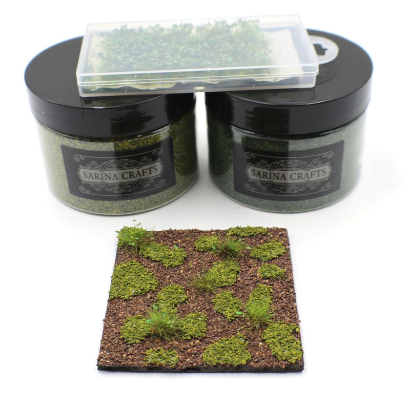 May include: Two glass jars with black lids and labels that say "Sarina Crafts" filled with green grass flock. A clear plastic container with a black lid filled with green grass flock. A brown square piece of foam with green grass flock glued on top.