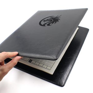 May include: A black leather-like portfolio folder featuring a debossed dragon emblem on the front cover. The folder is partially open, revealing an interior page with a grid layout and text labels including copper, silver, electrum, gold, and platinum.