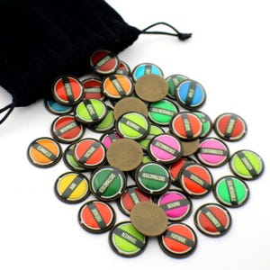 May include: A collection of game tokens with various status effects, including "Fatigue," "Shaken," and "Wounded." The tokens are round with a bronze finish and colorful backgrounds. A black velvet bag is partially visible.