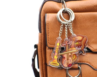 Puede incluir: Una bolsa de mensajero de cuero marrón con un llavero plateado con un encanto de clarinete, violín y piano.