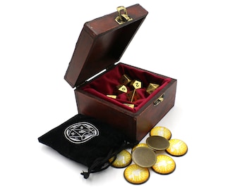 May include: A wooden box with a red velvet interior, containing a set of gold metal dice. The box is open and the dice are visible. There is also a black velvet bag with a white design and a set of gold metal tokens with a sun and a person design.
