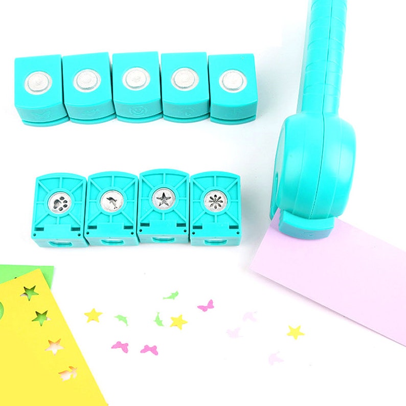 May include: A set of turquoise blue paper punch tools with different shaped cutouts. The tools are arranged in two rows. The top row has five round punches and the bottom row has four punches with different shapes, including a paw print, a bird, a star, and a flower. There are also several small paper cutouts scattered on a white surface.