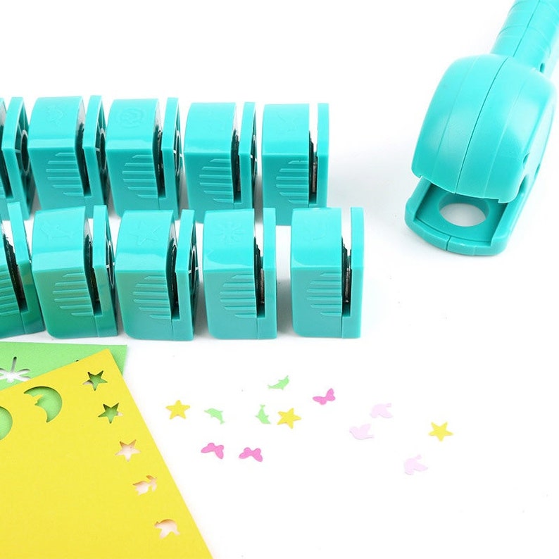 May include: A set of 12 turquoise blue paper punch tools with a matching turquoise blue paper punch tool with a handle. The tools are arranged in two rows of six. The tools are used to create different shapes in paper. The tools are on a white surface with a yellow piece of paper with cut out shapes in the background.