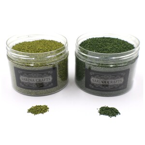 May include: Two clear plastic jars filled with green and light green craft moss. The jars have black labels with the text "Sarina Crafts".