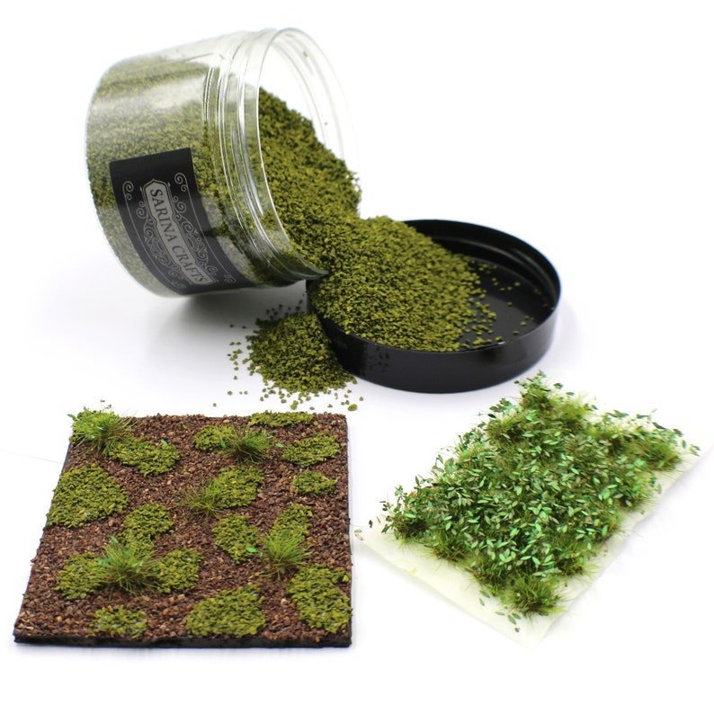May include: A clear jar filled with green grass flock, a black lid, and a small pile of green grass flock on a white surface. The jar has a black label with the text "SARINA CRAFTS". There are two samples of green grass flock on white paper.