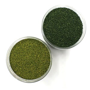 May include: Two clear glass jars filled with green and light green granular material. The jars are on a white background.