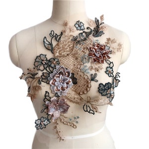 Könnte beinhalten: Eine zarte florale Applikation mit einem Mix aus beige, braun und blauen Tönen. Die Applikation zeichnet sich durch filigranes Spitzenwerk, Perlendetails und eine Vielzahl von Blütenformen aus.