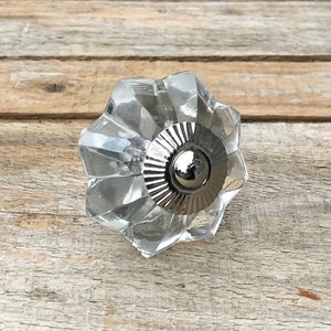 May include: A clear glass cabinet knob with a silver metal base. The knob has a faceted design and a starburst shape.