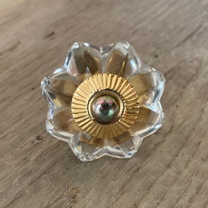 May include: A clear glass cabinet knob with a gold metal center. The knob has a flower-like design with a raised center.