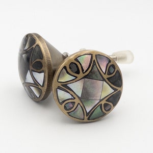 May include: Two brass cabinet knobs with a geometric design featuring black and iridescent mother-of-pearl inlay.