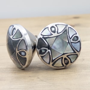 May include: Two round silver cabinet knobs with a geometric design made of black and white mother of pearl inlay.