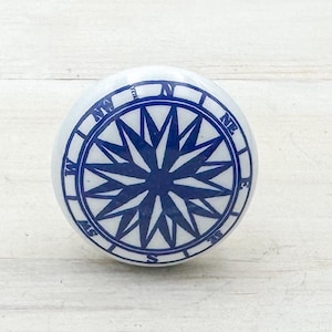 Peut inclure: Bouton de meuble en céramique blanche avec un motif de rose des vents bleu marine. Le bouton sur le thème nautique présente des marquages directionnels et un motif en étoile, idéal pour ajouter une touche de décoration côtière aux meubles.