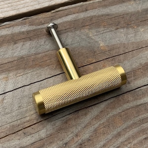 May include: A gold-toned cabinet knob with a textured, ridged surface. The knob has a screw on the top.