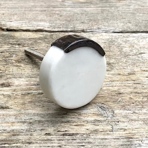 以下が含まれることがあります： 上部に茶色のアクセントが付いた白いセラミック製のノブ。ノブには銀色のネジが付いています。