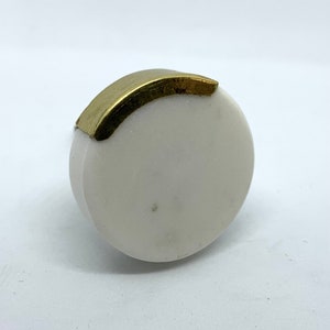 May include: A round white marble cabinet knob with a gold metal accent around the top edge.