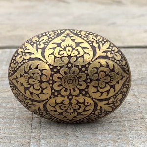 Peut inclure: Un bouton rond en laiton avec un motif floral décoratif, complexe et doré sur un fond brun foncé.