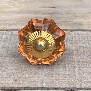May include: A peach-coloured glass cabinet knob with a gold metal centre. The knob has a starburst design.