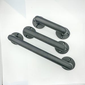 May include: Three black metal door pulls with a matte finish. Each pull has a rounded handle and a circular base with three screw holes for mounting. The hardware is arranged diagonally against a white background.
