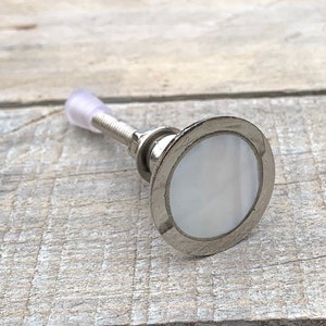 K&ouml;nnte beinhalten: Ein silberner Schrankknopf mit einer wei&szlig;en Perlmutteinlage. Der Knopf hat eine Schraube auf der R&uuml;ckseite zur Montage.