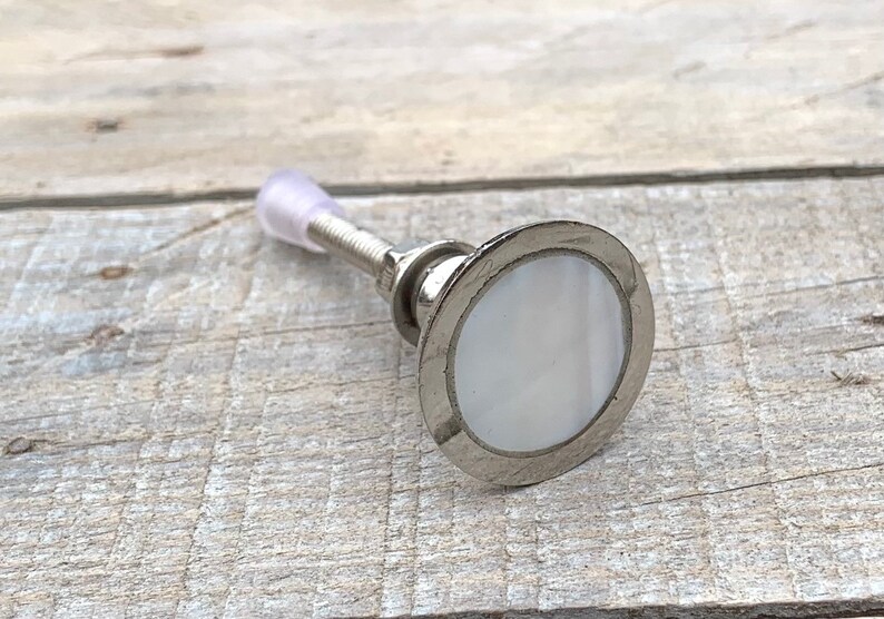 K&ouml;nnte beinhalten: Ein silberner Schrankknopf mit einer wei&szlig;en Perlmutteinlage. Der Knopf hat eine Schraube auf der R&uuml;ckseite zur Montage.