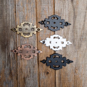 以下が含まれることがあります： 金、銅、白、黒の4種類の仕上げの装飾的な金属製ヒンジ。ヒンジは木製の背景に表示されています。