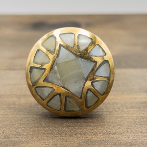 May include: A round, gold-toned cabinet knob with a geometric design featuring white mother-of-pearl inlay.