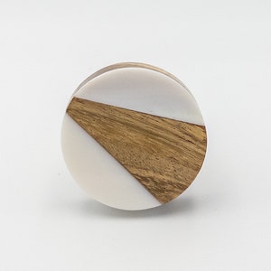 May include: Round wooden and white knob with a geometric design. The knob is made of wood and white resin.