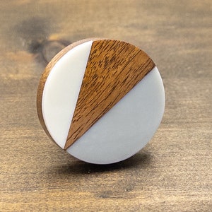 May include: A round wooden and white knob with a geometric design. The knob is made of two pieces of wood and white material.
