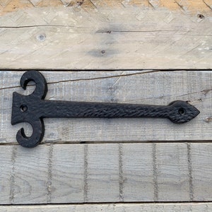 May include: Black metal hinge with a decorative design. The hinge is approximately 15 cm long and has a textured surface.