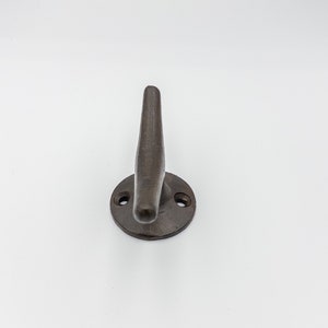 K&ouml;nnte beinhalten: Ein dunkelbrauner Metallhaken mit abgerundeter Basis und einem einzigen spitzen Haken. Der Haken ist an einer runden Basis mit zwei kleinen L&ouml;chern befestigt.