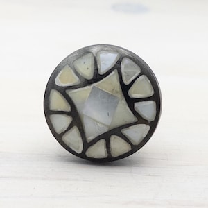May include: A round, black knob with a white, geometric design made of small, iridescent pieces. The knob has a smooth, polished finish.