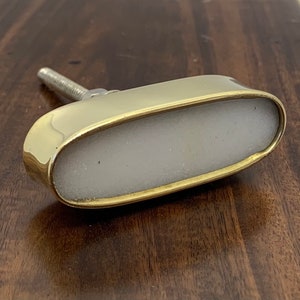 Peut inclure: Un bouton de porte ovale en or avec un centre blanc. Le bouton a une vis au dos.